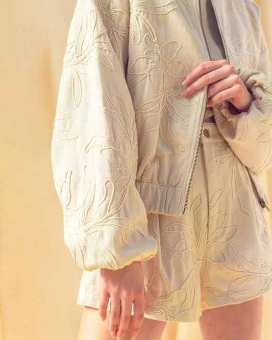 Light-colored embroidered jacket with floral patterns on a plain background