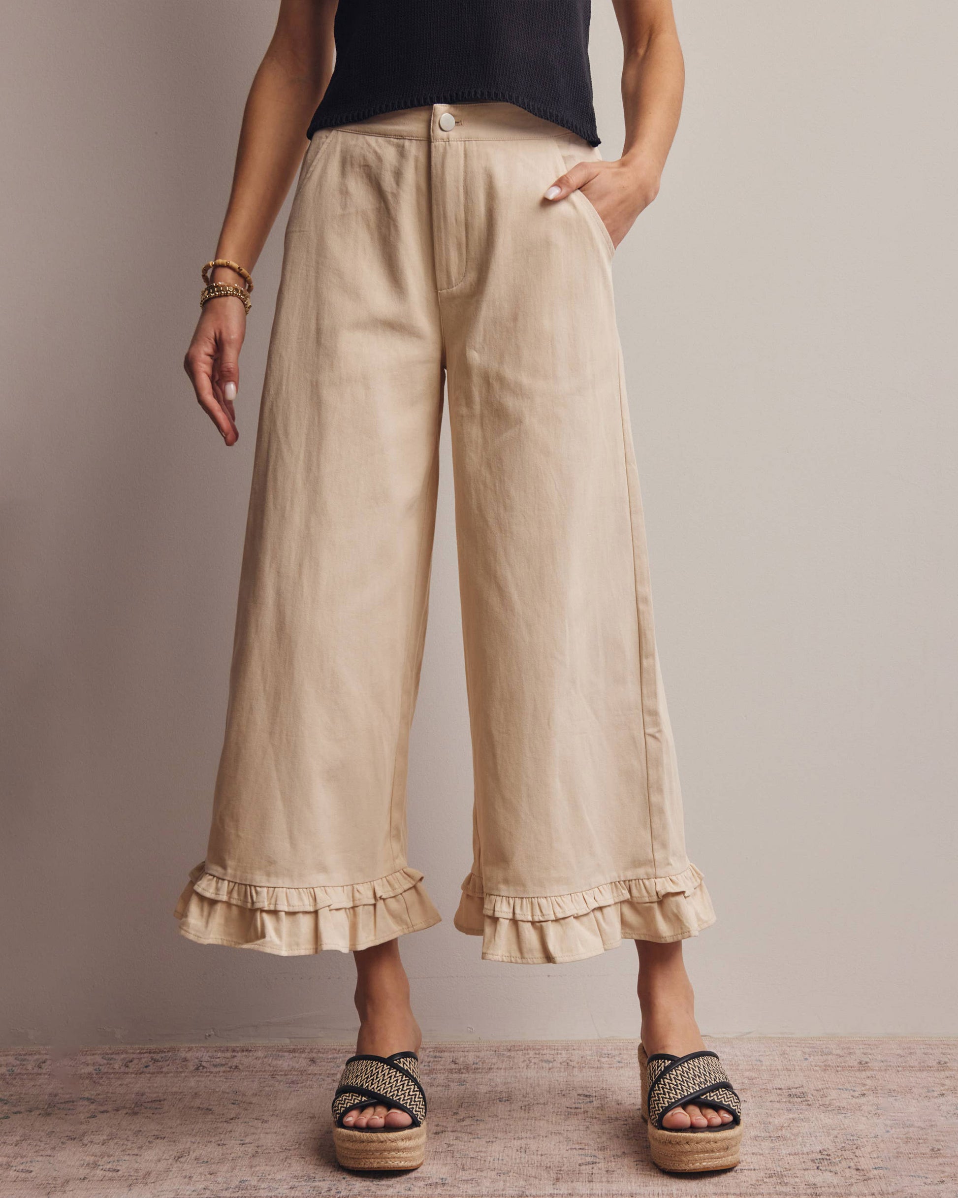 Beige wide-leg pants with ruffled bottom hem worn by a person on a neutral background