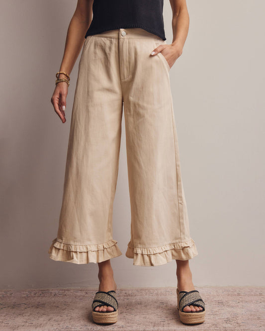 Beige wide-leg pants with ruffled bottom hem worn by a person on a neutral background