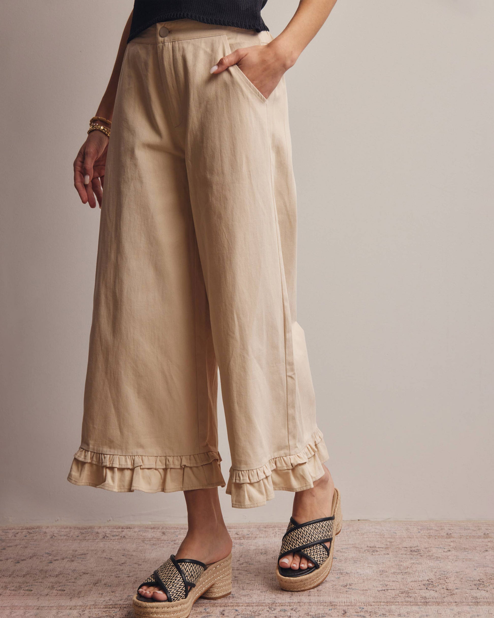 Person wearing beige ruffled pants with a neutral background