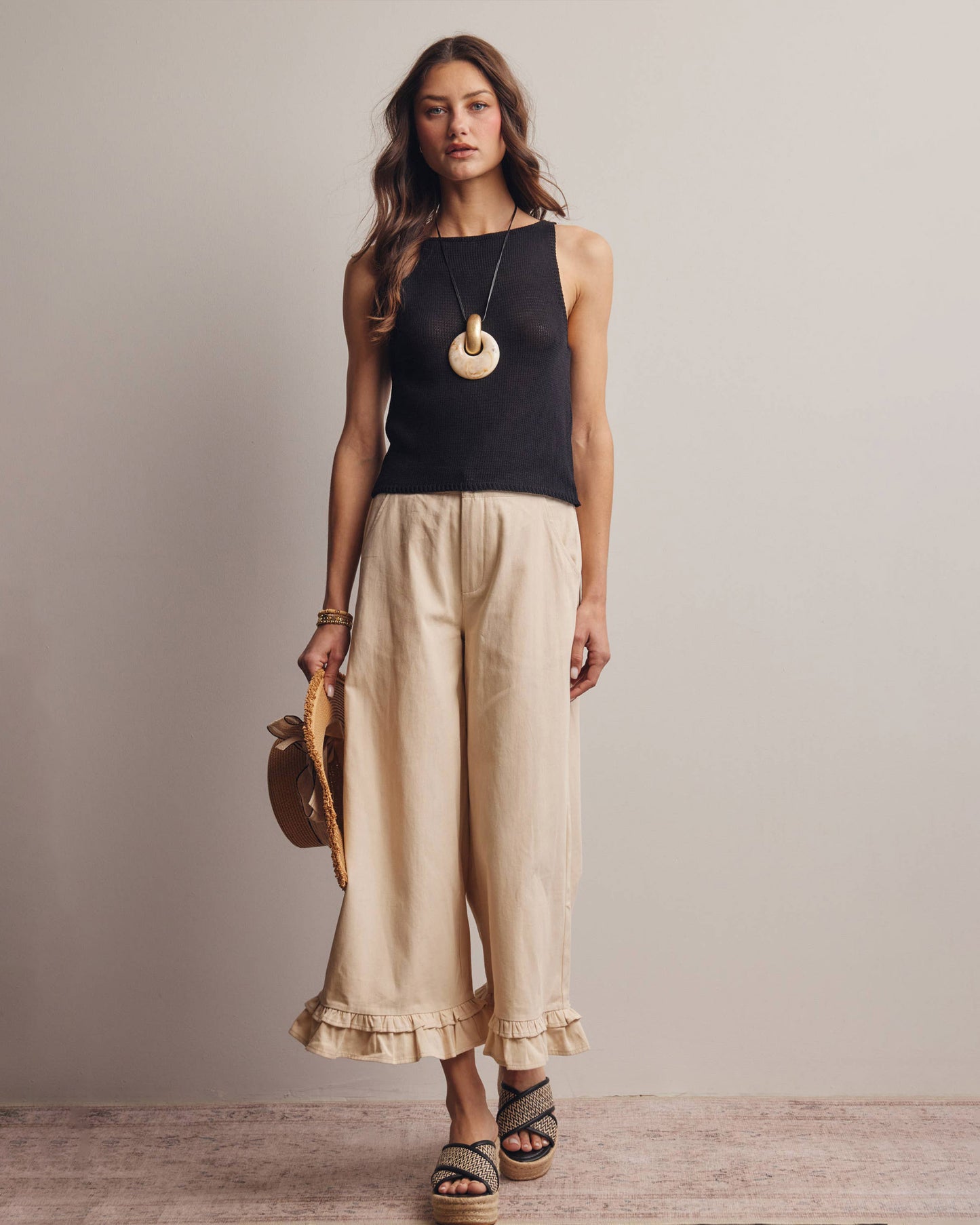 Woman wearing a black top and beige pants with a neutral background
