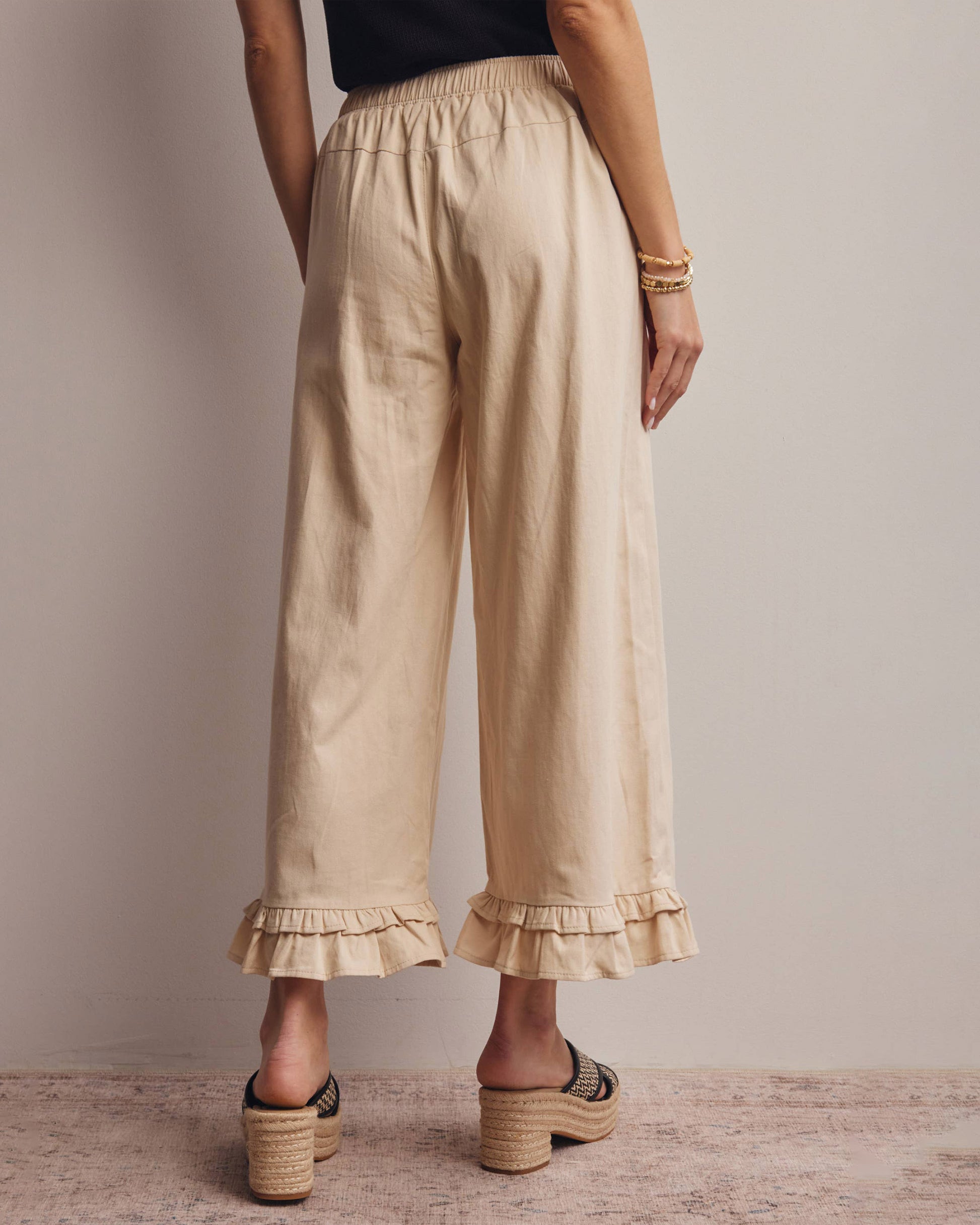 Beige ruffled pants worn by a person on a neutral background