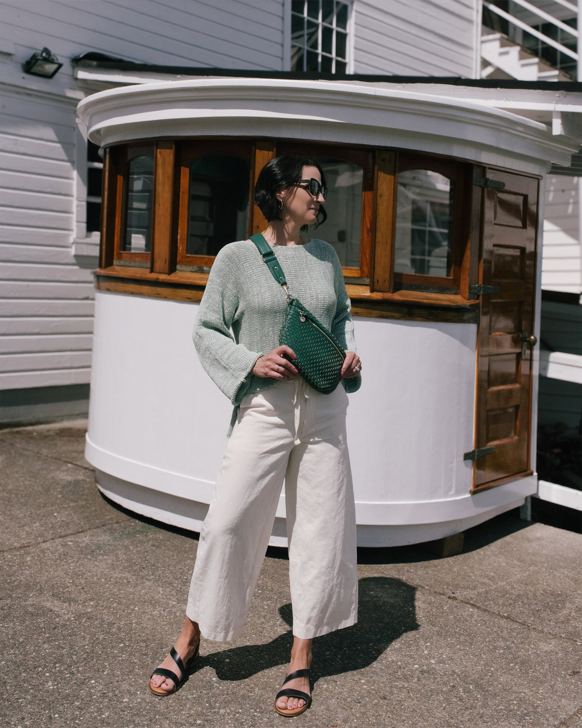 Woman holding a green bag in front of a white building with wooden doors.